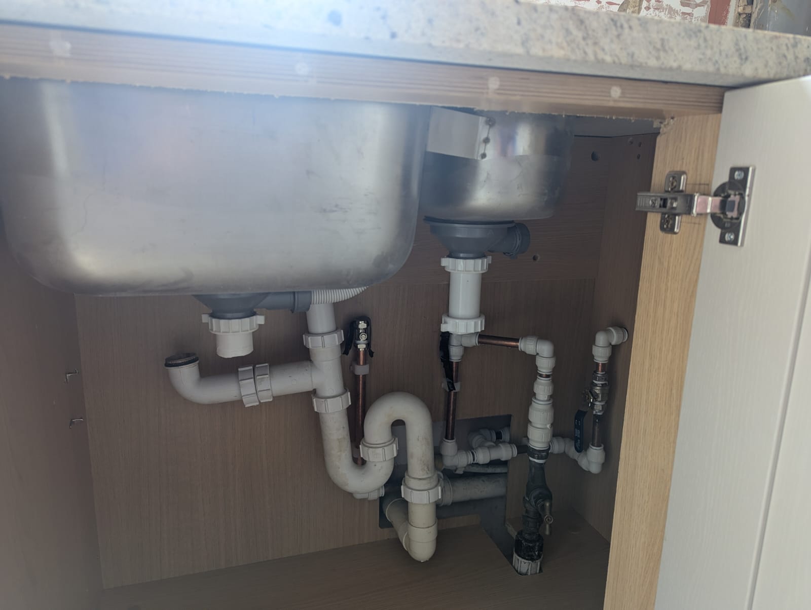 Neatly rebuilt waste and supply pipework beneath a double kitchen sink